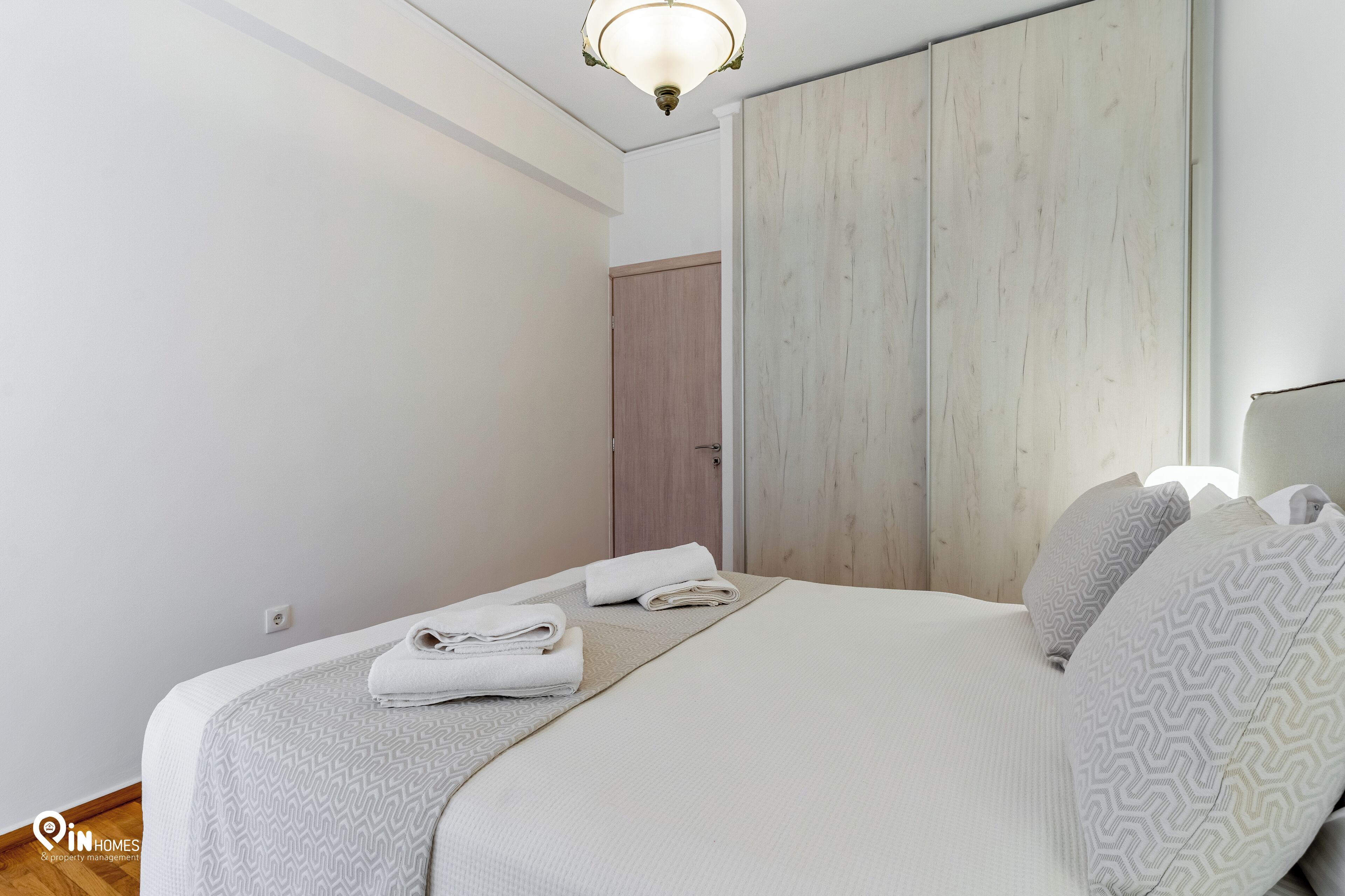 A neatly made bed with folded towels, a wooden wardrobe, and a light fixture.