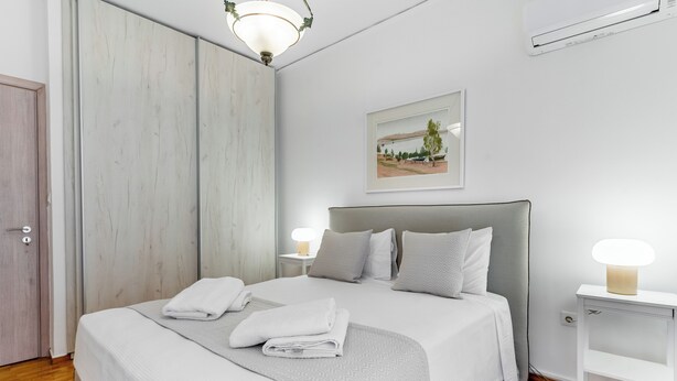 Une chambre à coucher moderne avec un grand lit, deux lampes de chevet, une table de chevet blanche et un tableau encadré au mur.