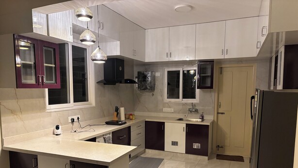 A modern kitchen with a central island, white cabinets, and pendant lighting. - The Yellow Gate - 2BHK - New Apartment - Near Banashankari (Bengaluru)