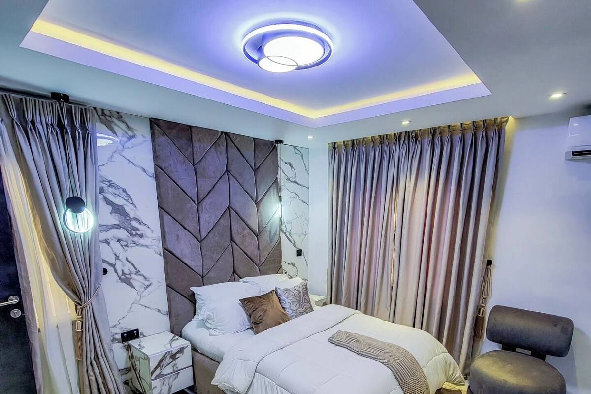 A modern bedroom with a bed, curtains, a nightstand, and a chair.