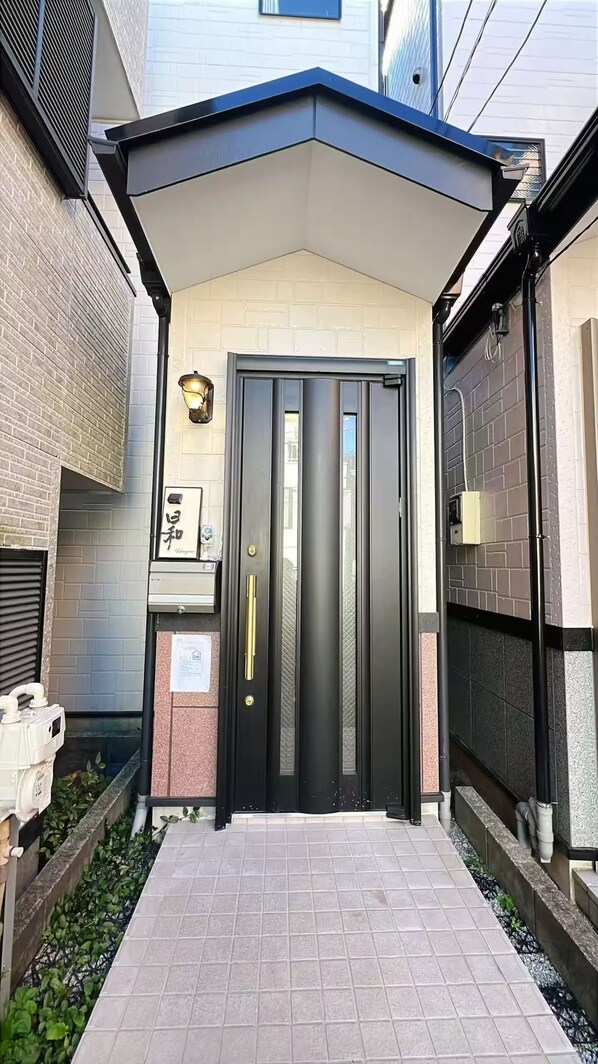 A modern entrance with a black door, a small garden area with plants, and a brick wall.