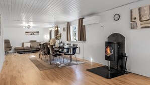 Un salon moderne comprenant un coin repas, un plancher en bois, une cheminée et une grande fenêtre avec des rideaux.