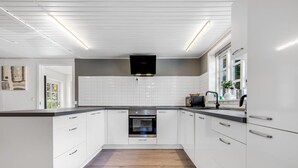 Une cuisine moderne avec des meubles blancs, un îlot central, un four encastré et une hotte noire.