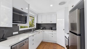 A modern kitchen with white cabinetry, a stainless steel refrigerator, a built-in microwave, and a coffee maker. - Sandy Feet Retreat - 1 Min To Beach (COPACABANA)