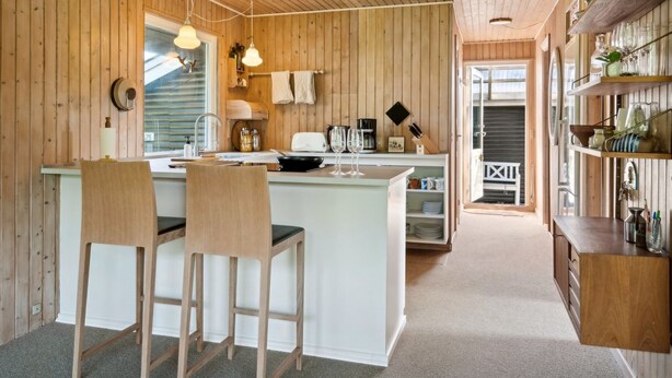A cozy kitchen with wooden walls and a central island, equipped with bar stools and a coffee machine. - "Roald" - 320m from the sea by Interhome (Otterup)