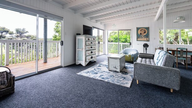 A spacious room with a large sliding glass door leading to a balcony, a grey sofa, a small table, and a white cabinet with drawers. - Kiwizone Hideaway. Full home- self checkin. (Kerikeri)