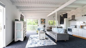 A cozy, well-lit room with a large window, a sofa, a small table, and a kitchenette area. - Kiwizone Hideaway. Full home- self checkin. (Kerikeri)