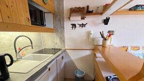 Una cocina compacta con armarios de madera, un lavamanos, un microondas y un pequeño cubo de basura.