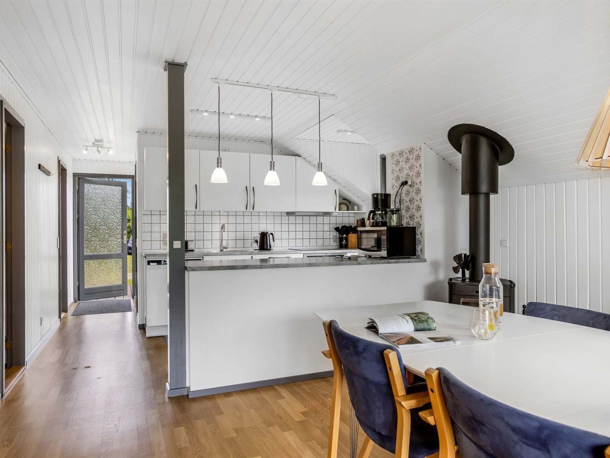 Una cucina moderna con mobili bianchi, un'isola centrale e illuminazione a sospensione.