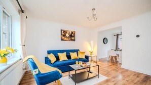 Un salon moderne avec un canapé bleu, des coussins jaunes, une table basse et un tableau accroché au mur.