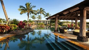 Piscina di un resort con palme, un'area lounge coperta e un edificio sullo sfondo.