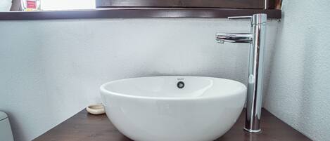 A white vessel sink with a chrome faucet on a wooden countertop, above a mirror with a wooden frame.