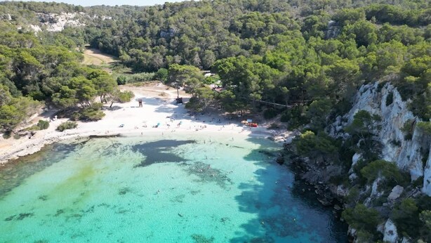 An aerial view of a beach with clear turquoise waters, surrounded by rocky cliffs and dense greenery. - Authentic Menorcan country house, close to the capital and beaches, in total calm. (Llucmaçanes)