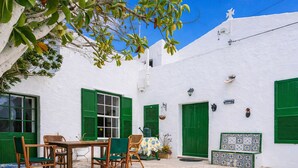 A white-walled building with green shutters, a tiled patio, and outdoor furniture. - Authentic Menorcan country house, close to the capital and beaches, in total calm. (Llucmaçanes)