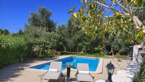 A swimming pool with two lounge chairs and a table, surrounded by greenery and trees. - Authentic Menorcan country house, close to the capital and beaches, in total calm. (Llucmaçanes)