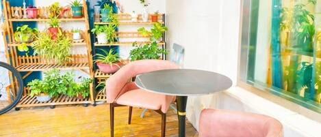 Een kamer met een ronde tafel, roze stoelen, een houten plantenplankje en uitzicht door een glazen raam.