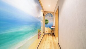 A narrow hallway with a mural of a beach scene, a desk with a computer, and a window with a view of a tree-lined island. - JinglaiHotel SouthBundXintiandi Branch (Shanghai)