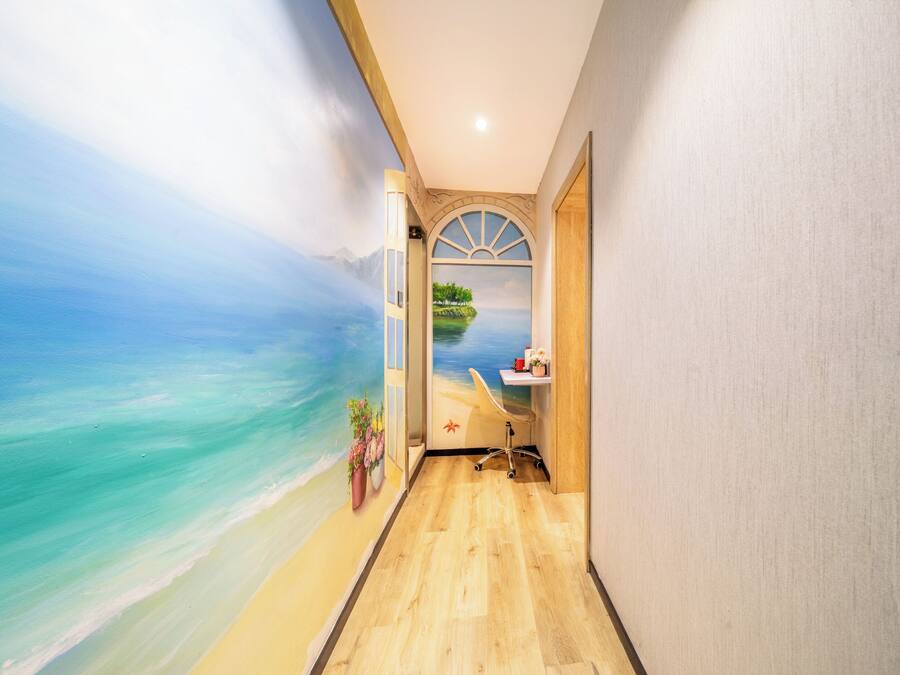 A narrow hallway with a mural of a beach scene, a desk with a computer, and a window with a view of a tree-lined island.
