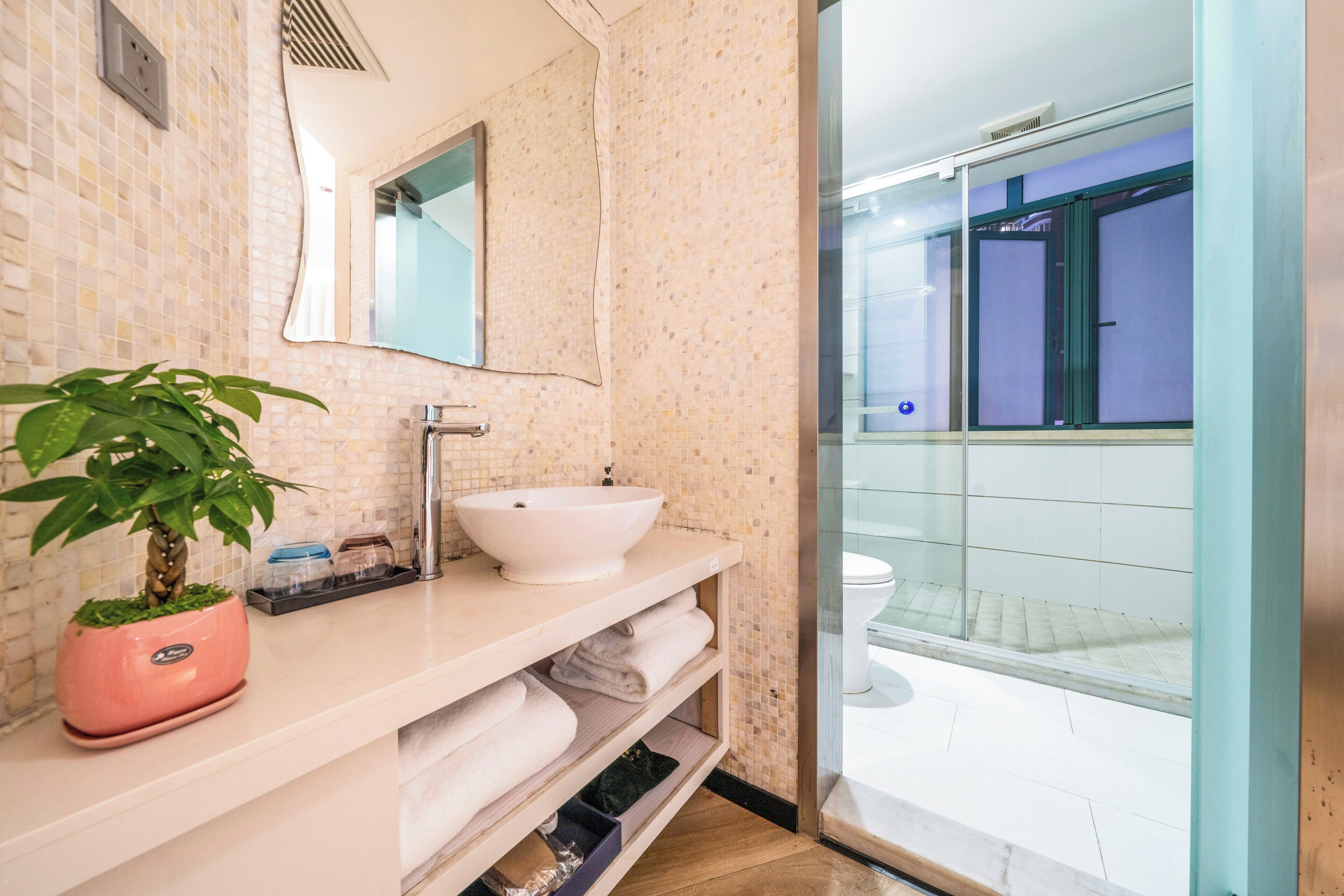 Ein modernes Badezimmer mit einem weißen Waschbecken, einem Spiegel und einer Topfpflanze.