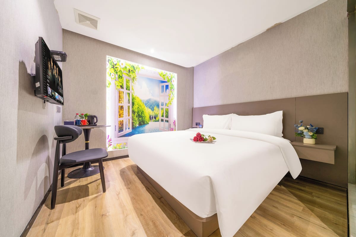 Habitación de hotel moderna con una cama grande, un escritorio con una silla, un televisor de pantalla plana y una ventana con vistas a zonas verdes.