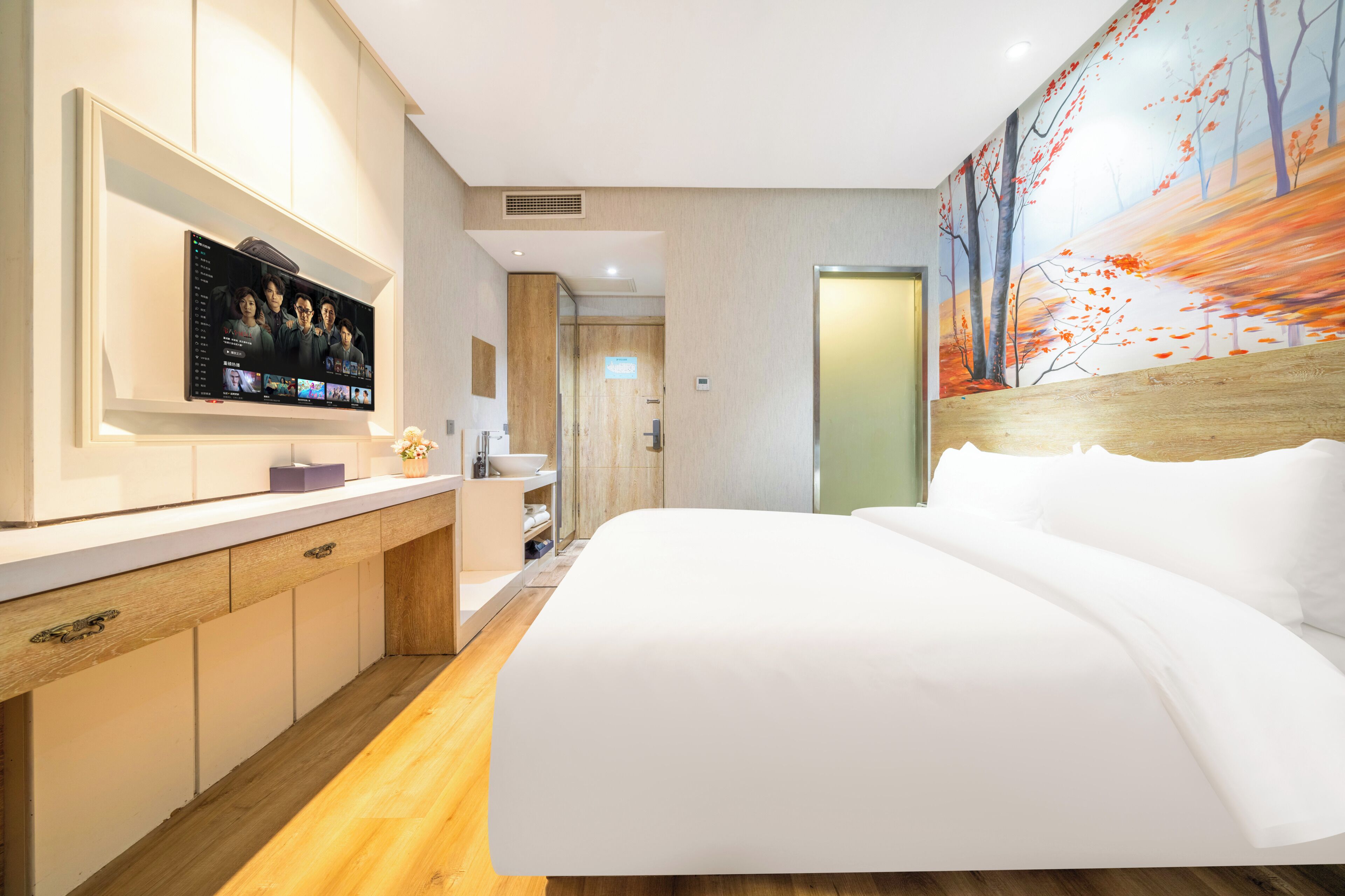 Quarto de hotel moderno com uma cama grande, televisão fixada na parede, piso de madeira e um quadro na parede.