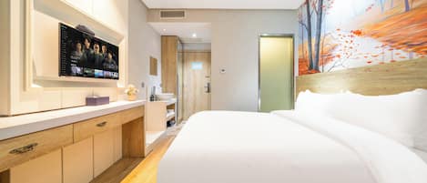 A modern hotel room with a large bed, a TV mounted on the wall, a wooden floor, and a painting on the wall.