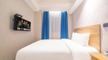 A hotel room with a large bed, a TV mounted on the wall, and a wooden headboard.