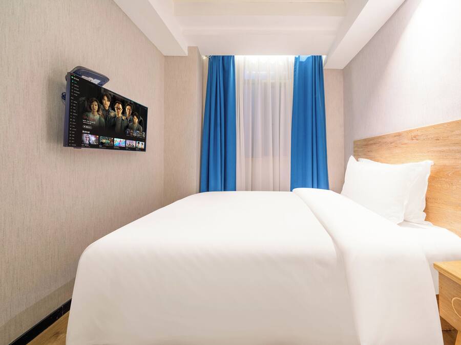A hotel room with a large bed, a TV mounted on the wall, and a wooden headboard.