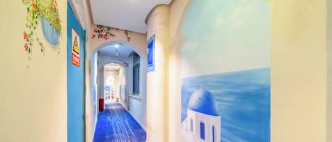 A hallway with a blue carpet, a mural of a blue sky and white building, and a warning sign on the wall.