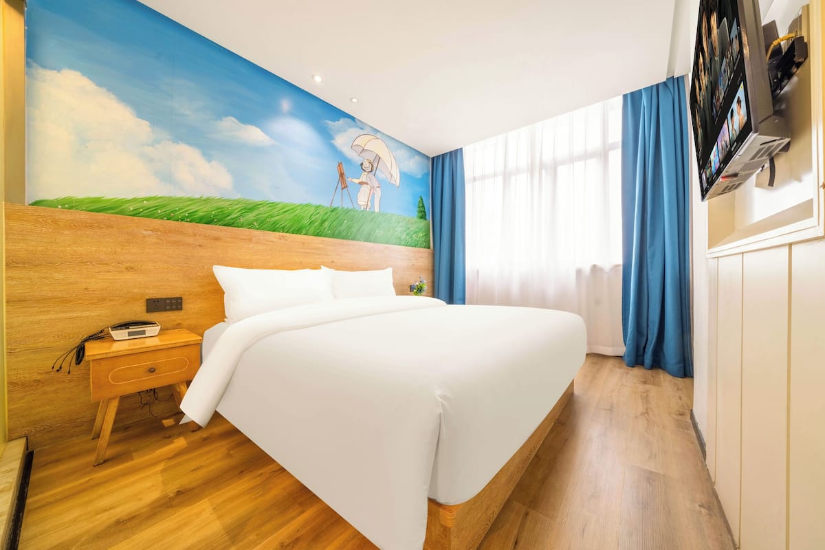 Un dormitorio con cabecera de madera, cama con ropa de cama blanca, un mural en la pared y un televisor montado en la pared.