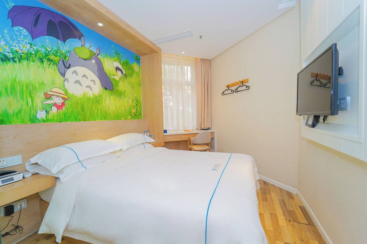Habitación de hotel con cama, escritorio, silla, televisor y un mural en la pared.