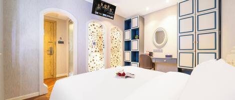 A modern hotel room with a large bed, a TV mounted on the wall, a desk with a chair, and a mirror.