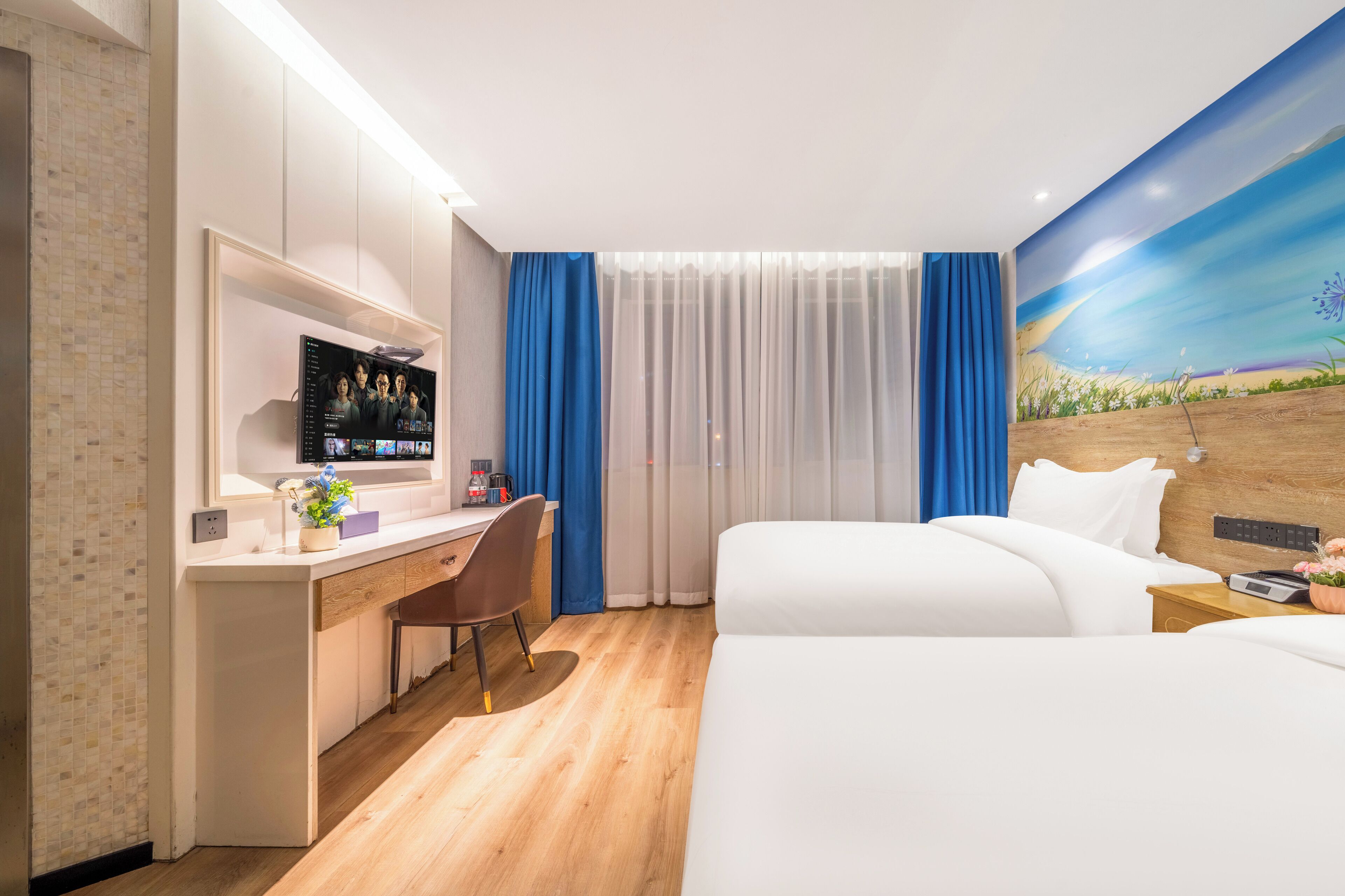 A hotel room with a bed, a desk with a computer, a chair, and a large window with curtains.