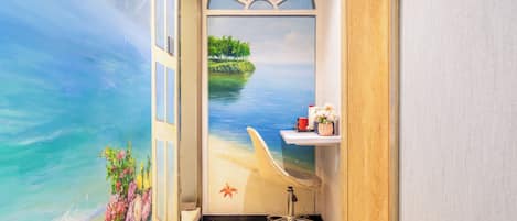 A room with a beach mural, a wooden desk, a chair, and a potted plant.