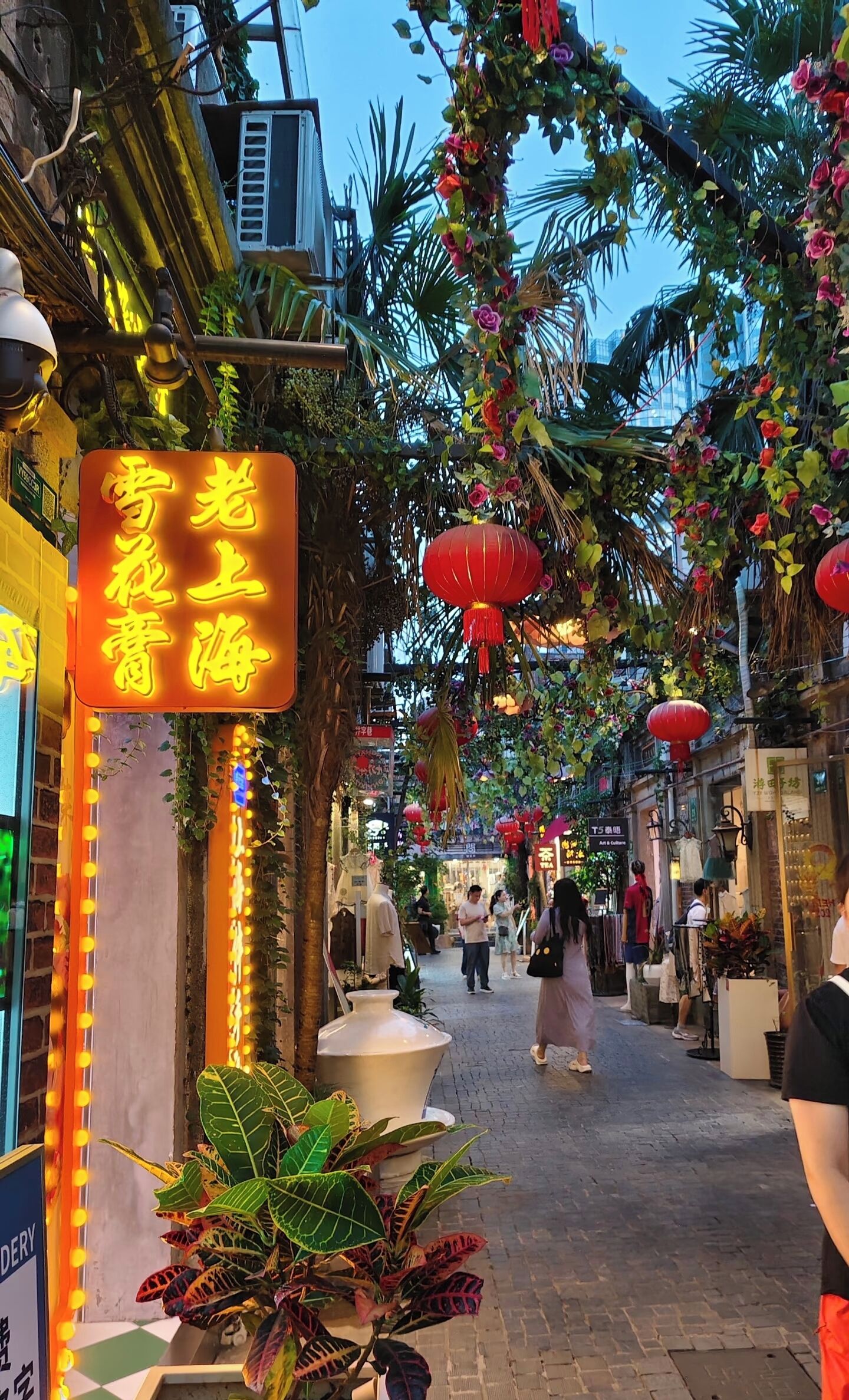 A street with shops, a neon sign, and hanging decorations.
