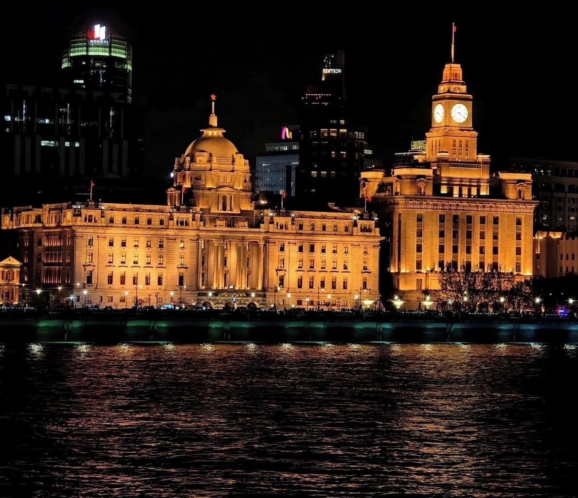 A large, historic building with a prominent clock tower and a dome, situated by a body of water.