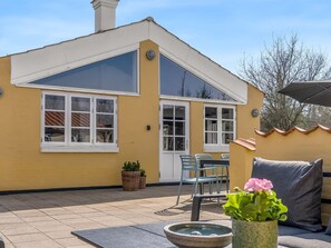 Un bâtiment jaune doté d’une grande fenêtre, d’une porte et d’un patio aménagé avec des chaises et une table.