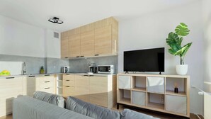Eine moderne Küche mit hellen Holzschränken, einer grauen Arbeitsplatte und einem Flachbildfernseher auf einem Holzboden.
