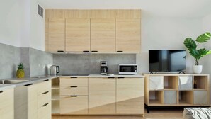 Eine moderne Küche mit hellen Holzschränken, einer Edelstahl-Spüle, einer Kaffeemaschine, einer Mikrowelle und einem Fernseher auf einem Holzboden.
