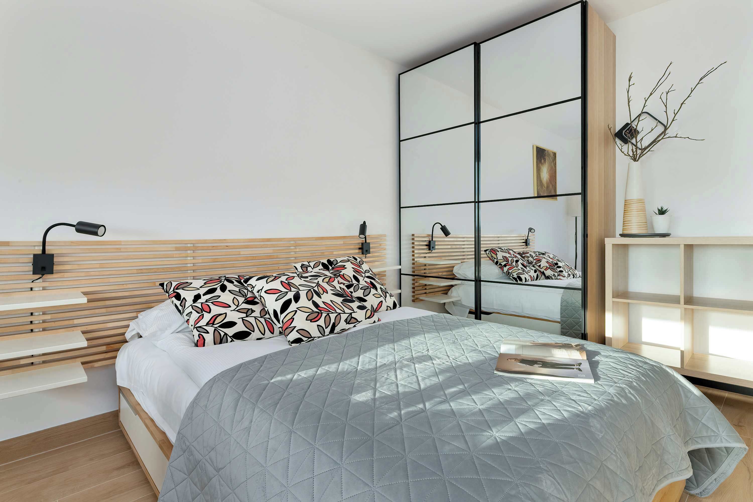 Une chambre à coucher moderne avec un lit, des tables de chevet, un miroir et un vase décoratif.