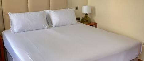 A neatly made bed with white linens, a headboard, and a bedside table with a lamp.