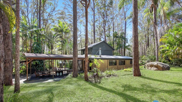 Une maison entourée de grands arbres et dotée d’un espace extérieur abrité, avec des tables et des chaises.