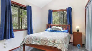 Une chambre à coucher avec un lit, une table de chevet, une lampe et une fenêtre avec des rideaux.