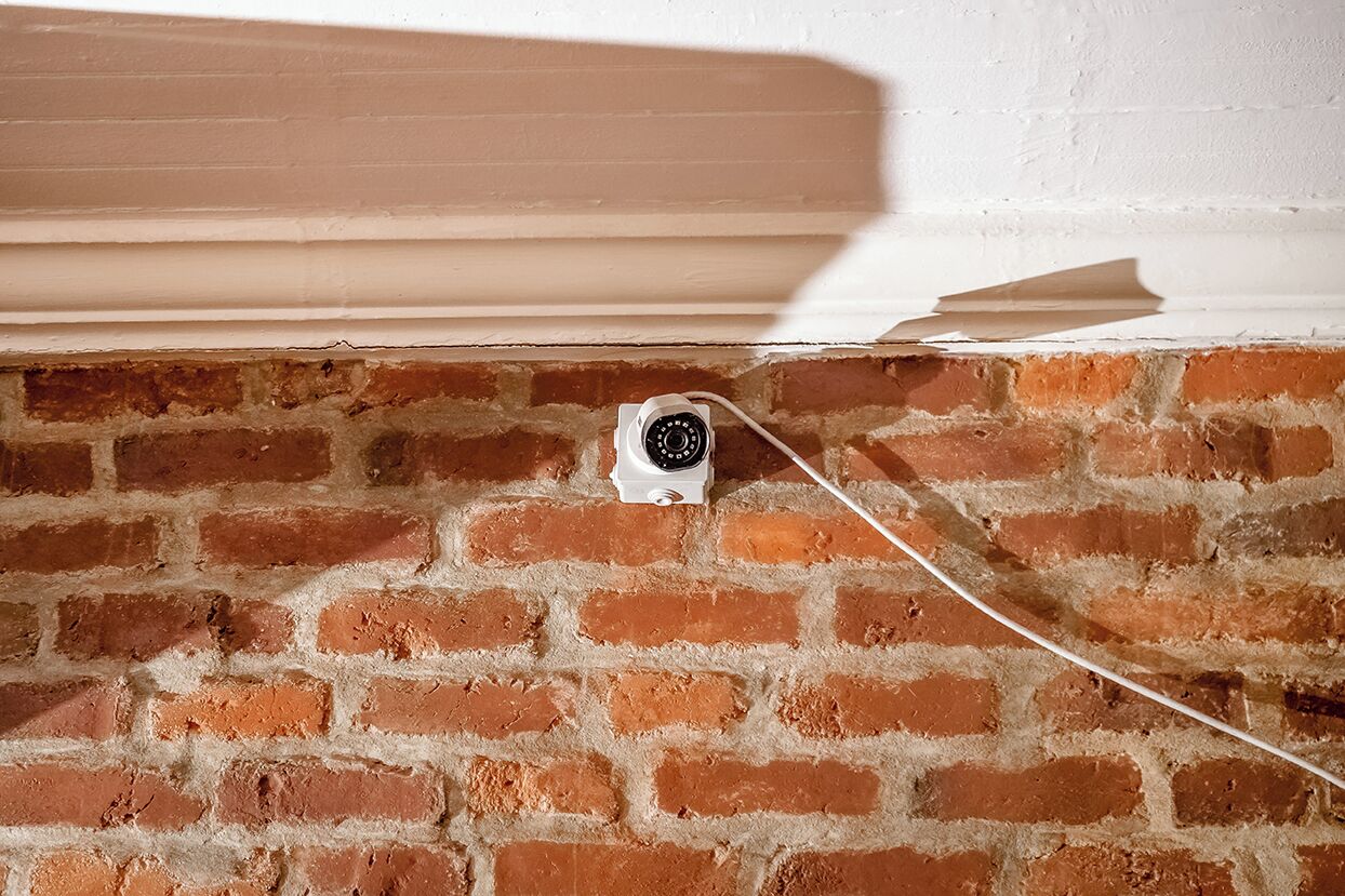 Una cámara de seguridad montada en una pared de ladrillo, conectada a un cable blanco.