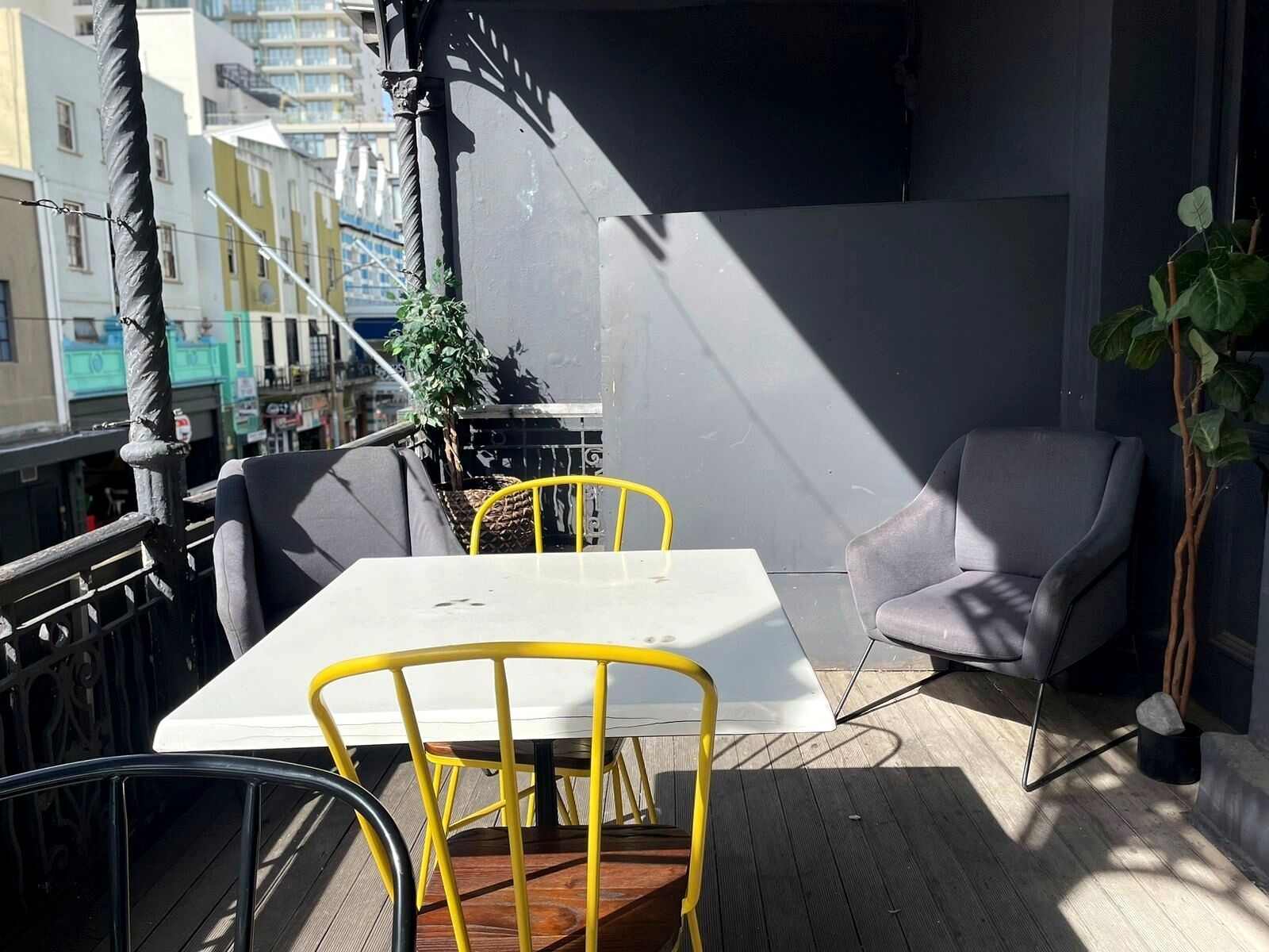 An outdoor seating area with a table and chairs, a potted plant, and a view of buildings in the background.