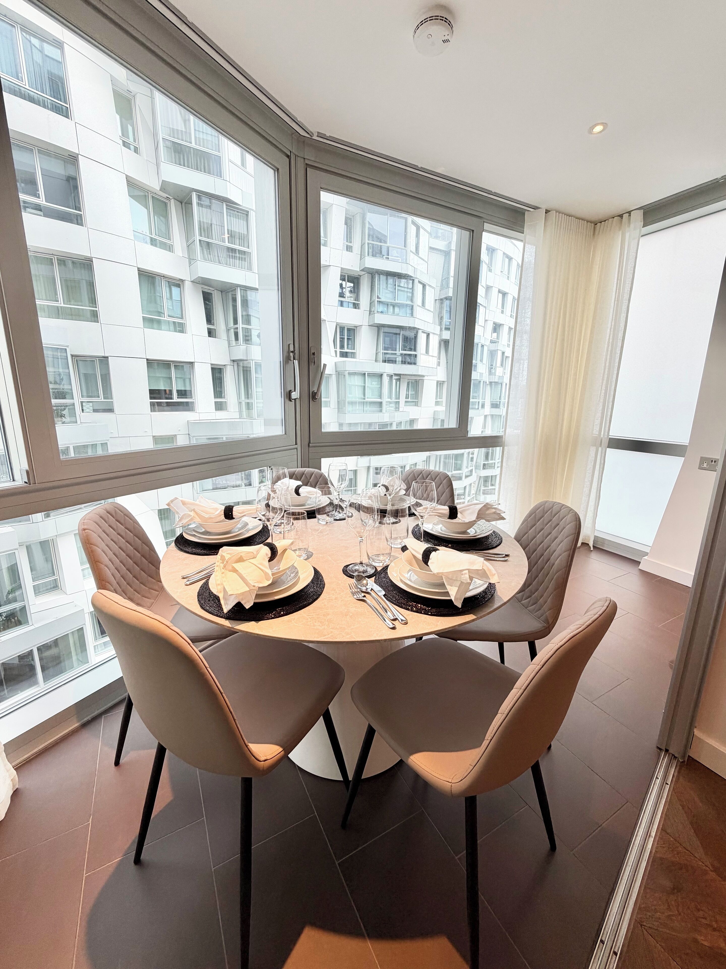 A dining area with a round table set for four, large windows, and a view of a high-rise building.