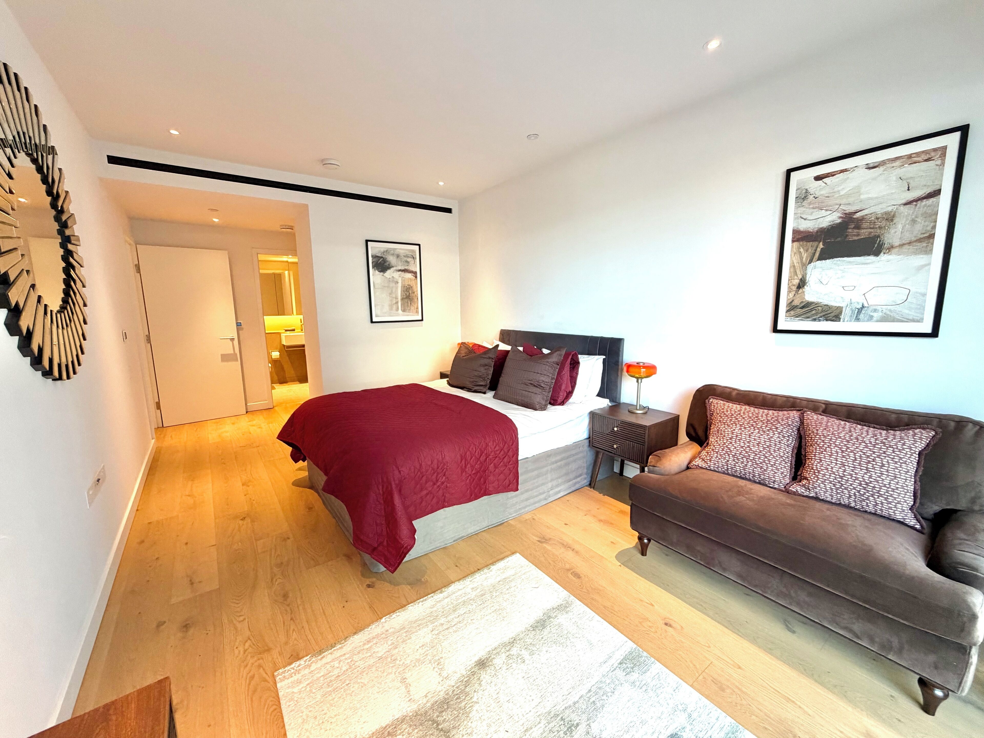 A modern bedroom with a large bed, a brown sofa, and a wooden floor.