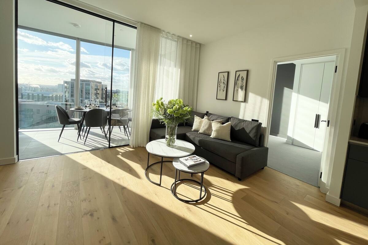 A modern living room with a dining area, large windows, and a city view.