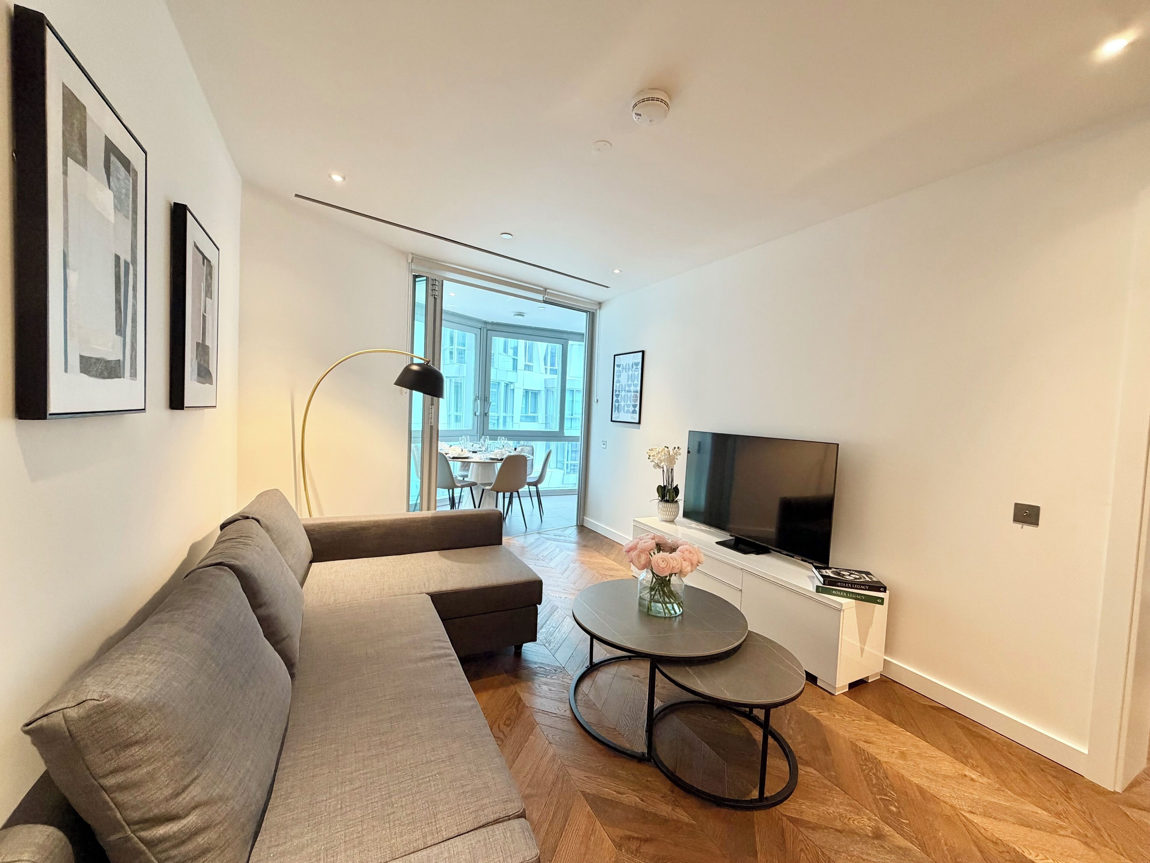 A modern living room with a grey sofa, a round coffee table, a TV, and a bookshelf.