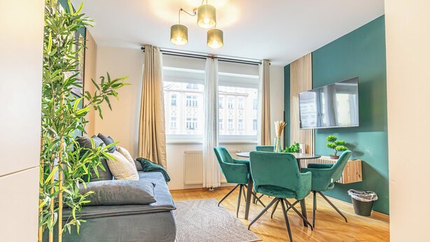 Ein modernes Wohnzimmer mit einer Couch, grünen Sesseln, einem Esstisch und einem an der Wand befestigten Fernseher.